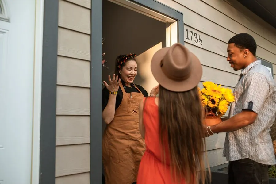 Una anfitriona recibiendo a unos huéspedes en la puerta con flores